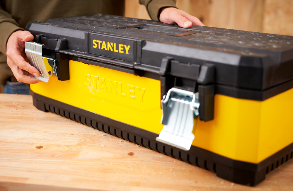 Skrzynka narzędziowa STANLEY Żółta 1-95-614 zbliżenie na zamki osoba otwiera skrzynię dwa solidne metalowe zamki bezpieczne przechowywanie narzędzi i akcesoriów ochrona zawartość przed przypadkowym otwarciem trwałość