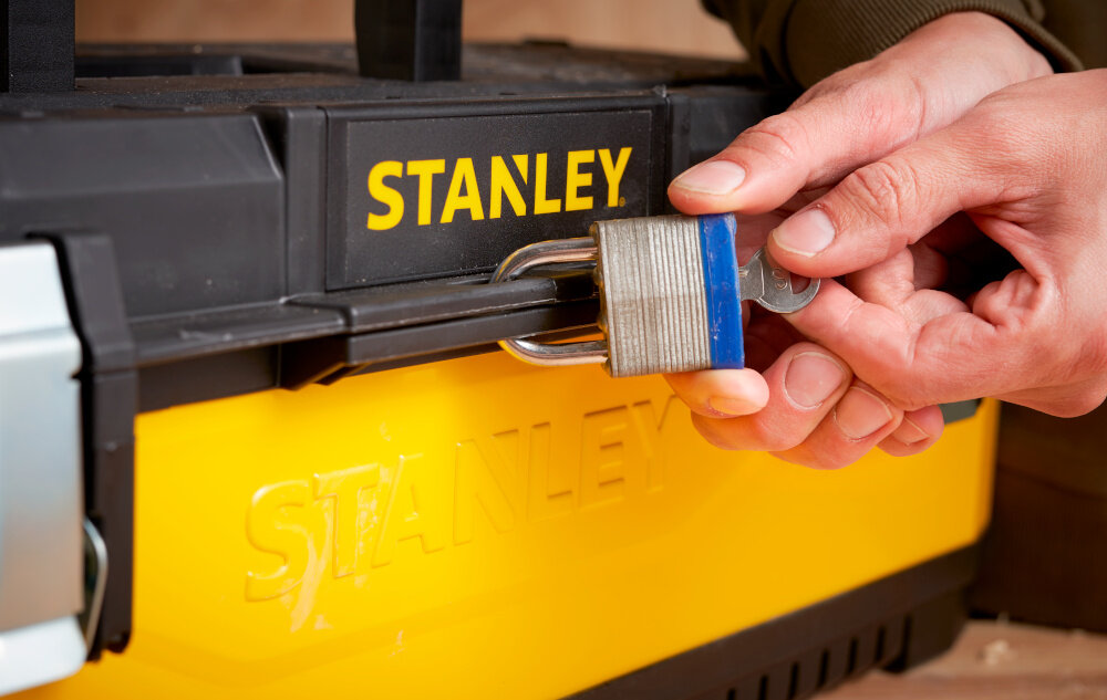 Skrzynia narzędziowa STANLEY 1-95-614 zbliżenie na otwór do kłódki osoba zakłada kłódkę na skrzynię otwór umożliwiający założenie kłódki bezpieczeństwo przechowywanych narzędzi