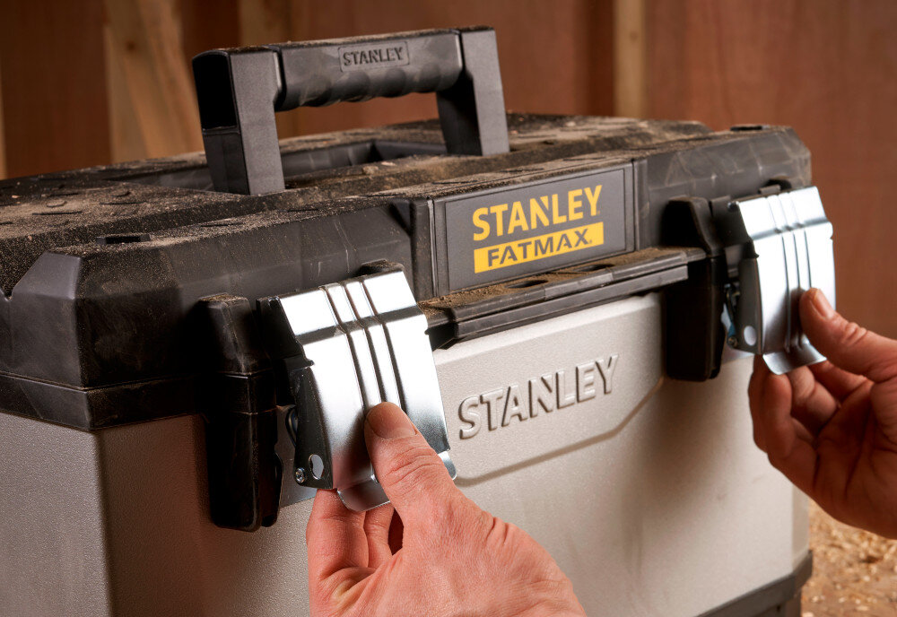 Skrzynka narzędziowa STANLEY Fatmax 1-95-617 zbliżenie na zamki osoba otwiera skrzynię dwa solidne metalowe zamki bezpieczne przechowywanie narzędzi i akcesoriów ochrona zawartość przed przypadkowym otwarciem trwałość