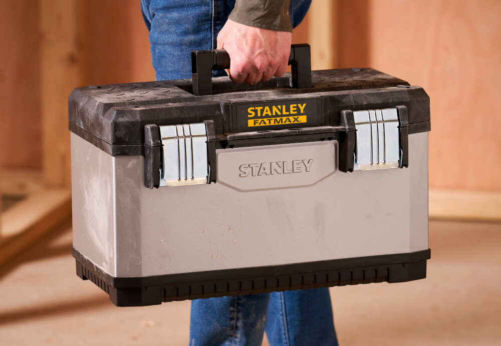 Skrzynka narzędziowa STANLEY Fatmax 1-95-617 osoba niesie skrzynię w dłoni w tle drewniana ściana duża rękojeść z wysokiej jakości tworzywa sztucznego stabilny chwyt komfort przenoszenia ergonomiczny kształt pewnie leży w dłoni nie ślizga się w czasie transportu metalowe zatrzask i zawiasy trwałość i pewne zamykanie udźwig do 28 kg możesz przenosić pełny zestaw sprzętu w jednym miejscu