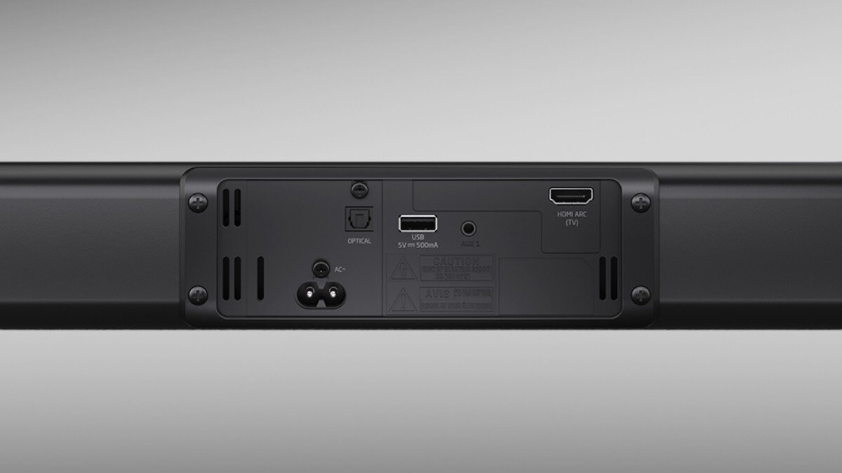 Tył czarnego soundbara z widocznymi portami: zasilania, optycznym, USB, AUX i HDMI ARC. Obok portów znajdują się oznaczenia i symbole techniczne.