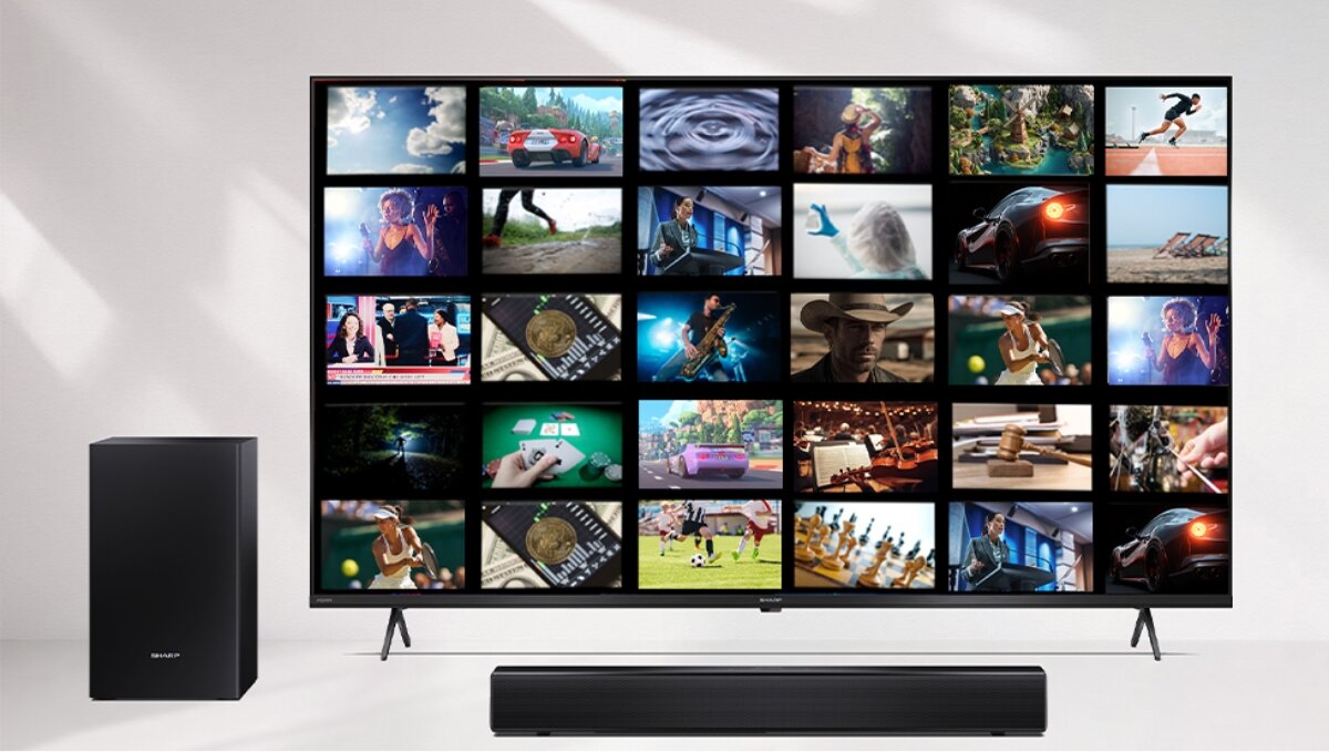 Na obrazie znajduje się duży telewizor z wyświetlonymi miniaturami różnych scen filmowych oraz czarny soundbar i subwoofer. Na subwooferze widoczne jest logo \'SHARP\'.