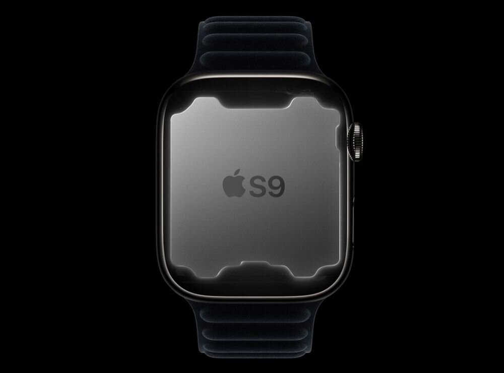 Na obrazie widoczny jest zegarek z ciemnym paskiem i srebrną kopertą. Na ekranie zegarka znajduje się logo Apple oraz napis \'S9\'.