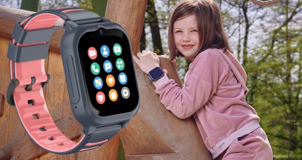 Na zdjęciu widoczny jest smartwatch z kolorowym wyświetlaczem, na którym znajdują się różne ikony aplikacji. Obok znajduje się dziecko w różowym stroju, wspinające się na drewnianą konstrukcję, również noszące smartwatch na nadgarstku.