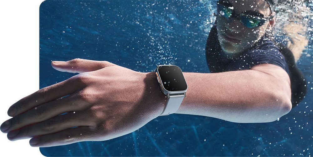 Osoba pływa w basenie, mając na nadgarstku czarny smartwatch z prostokątnym wyświetlaczem. W tle widać wodę basenową.