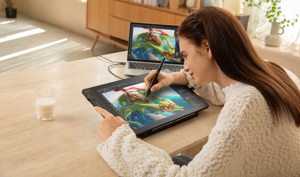 Tablet HUION Kamvas 16 gen. 3
							wygodne tworzenie treści, kobieta rysująca na tablecie, tablet, laptop oraz szklanka z napojem na biurku