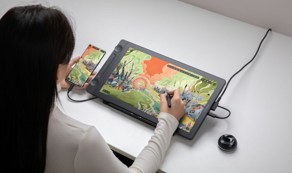 Tablet HUION Kamvas 16 gen. 3
					szczegółowy obraz, ekran IPS LCD o przekątnej 15,8 cala i rozdzielczości 2560 x 1440 pikseli,
					pełna laminacja, barwy odwzorowane zgodnie ze 120% palety sRGB, matowe szkło, współczynnik ΔE<1,5, każdy egzemplarz jest indywidualnie kalibrowany,
					białe biurko, osoba rysująca na tablecie oraz trzymająca smartfon w ręce