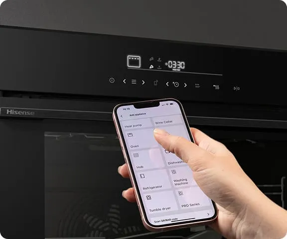 Osoba trzyma smartfon z aplikacją do sterowania urządzeniami, przed czarnym piekarnikiem z wyświetlaczem pokazującym czas 03:30. Na piekarniku widoczne jest logo \'Hisense\'.