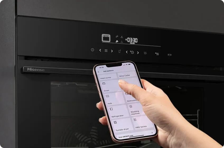 Osoba trzyma smartfon z aplikacją do sterowania urządzeniami, przed czarnym piekarnikiem marki Hisense z wyświetlaczem pokazującym czas 0:33:0. Na ekranie telefonu widoczne są opcje takie jak \'Oven\', \'Hob\', \'Refrigerator\'.