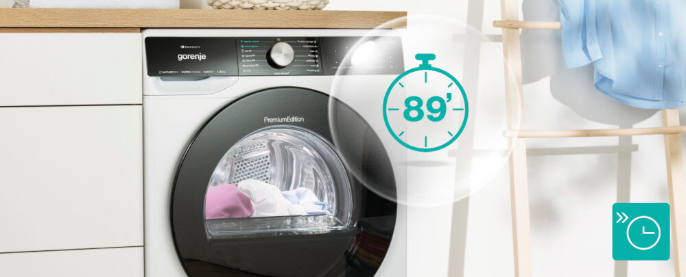 Na obrazie widoczna jest suszarka Gorenje z napisem \'Premium Edition\' na drzwiczkach, obok której znajduje się symbol zegara z liczbą \'89\'. W tle widać fragment szafki i wieszak z niebieską koszulą.