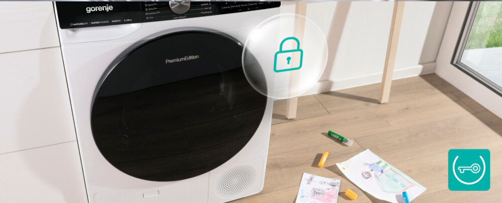 Na zdjęciu widoczna jest suszarka marki gorenje z napisem \'Premium Edition\' na drzwiach. Obok suszarki leżą kolorowe kredki i kartki papieru, a na obrazie znajduje się symbol kłódki.