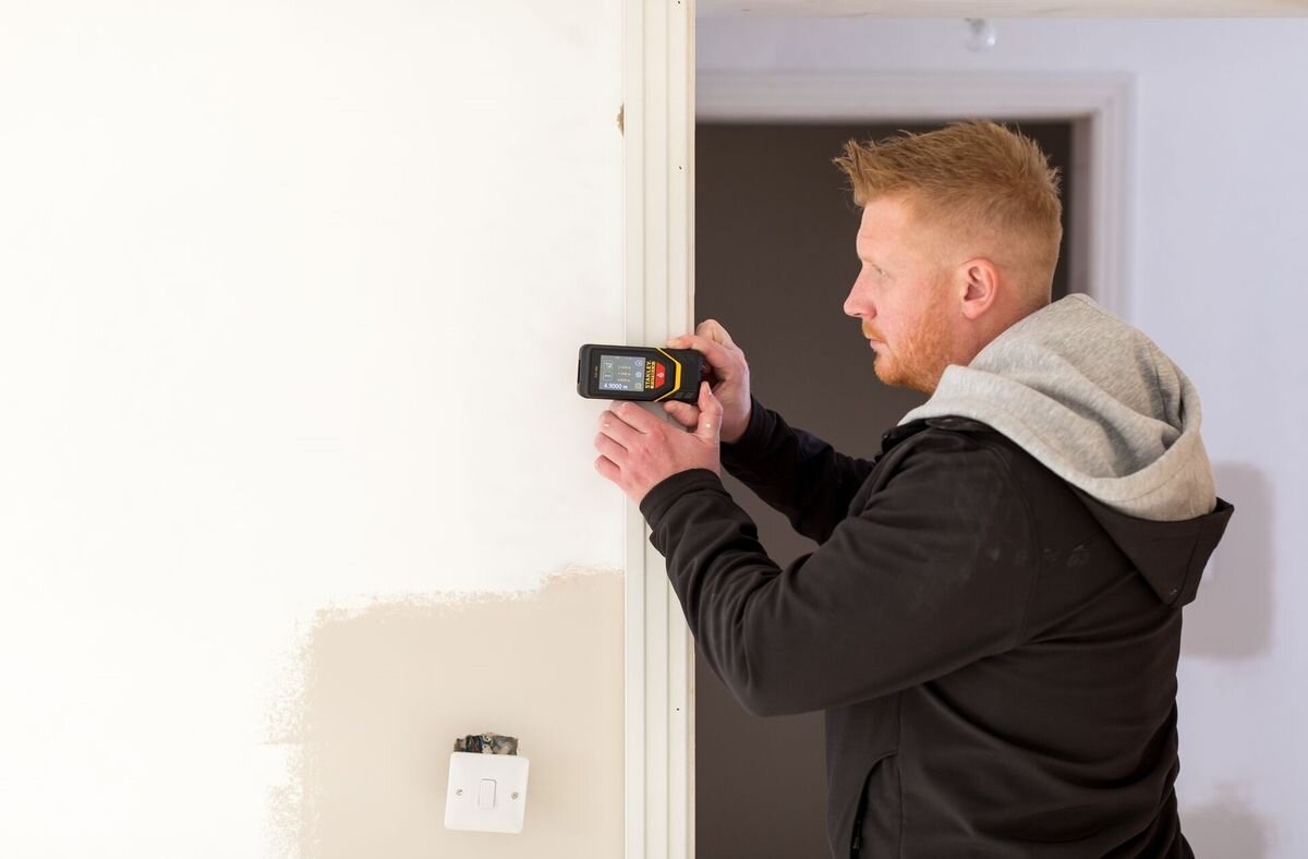 Dalmierz laserowy STANLEY TLM 165S STHT1-77139 50m, pamięć, timer, wyświetlacz, chwyt, mężczyzna odmierza laserem dystans w remontowanym pomieszczeniu