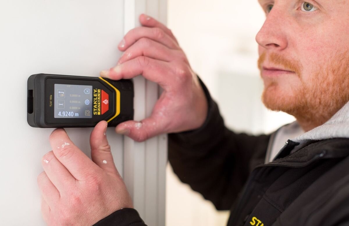 Dalmierz laserowy STANLEY TLM 165S STHT1-77139 50m, obudowa, ekran, przycisk, statyw, mężczyzna odmierza laserem dystans w remontowanym pomieszczeniu