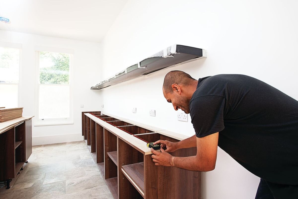 Dalmierz laserowy STANLEY TLM 165S STHT1-77139 50m, baterie, oszczędzanie, wiązka, energia, mężczyzna odmierza laserem dystans w remontowanym pomieszczeniu