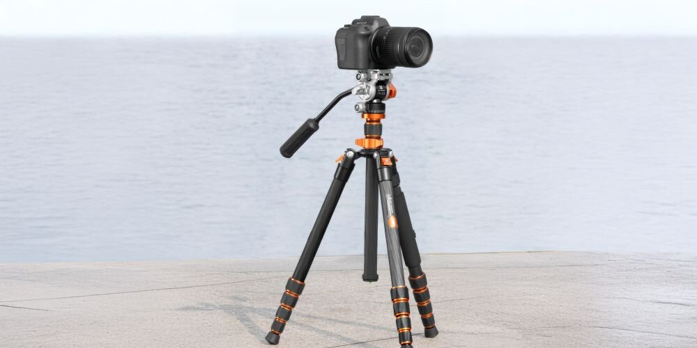Statyw video K&F Concept O255C4 z głowicą FH-03 i zamontowaną na nimlustrzanką na plaży na tle spokojnego morza