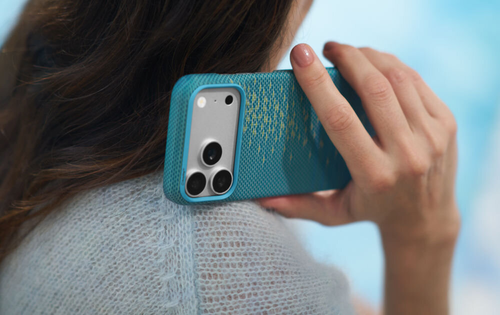 Osoba trzyma telefon z niebieskim etui z widocznymi trzema obiektywami aparatu. Etui ma teksturę i złote wzory na powierzchni.