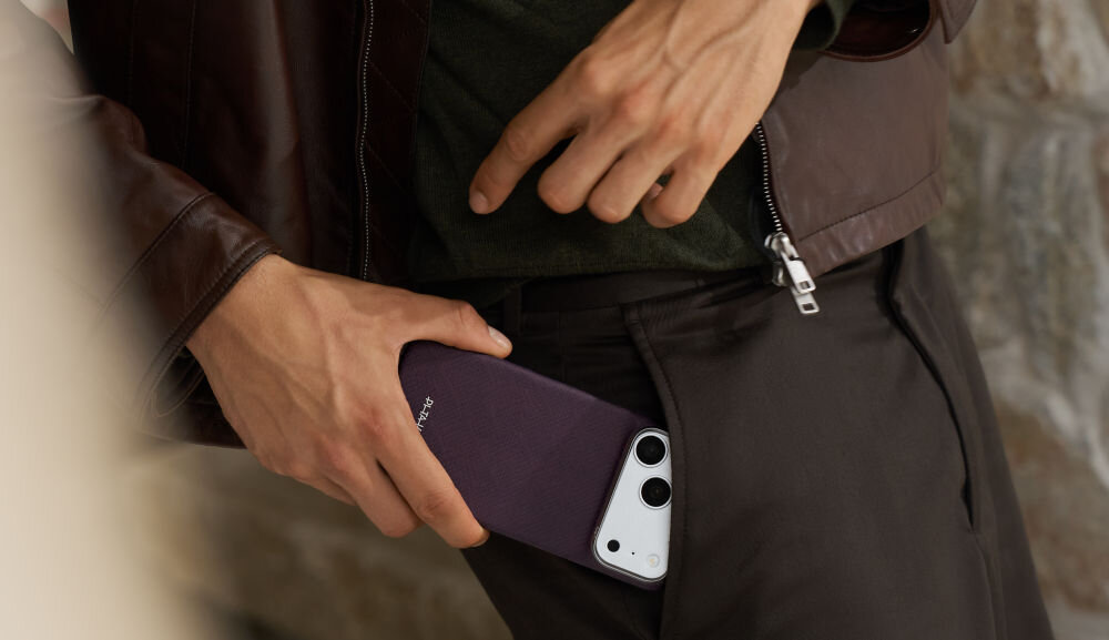 Osoba wkłada fioletowe etui na telefon do kieszeni spodni. Na etui widoczny jest napis \'PITAKA\'.