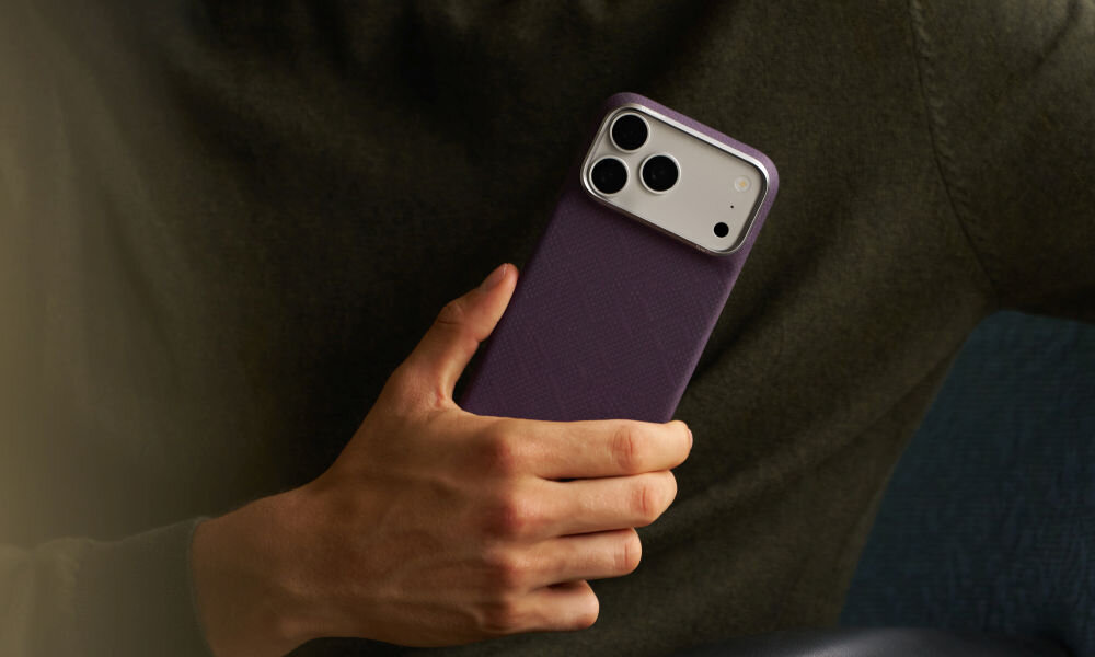 Osoba trzyma telefon w fioletowym etui z trzema widocznymi obiektywami aparatu. Etui ma teksturę i jest dopasowane do kształtu telefonu.