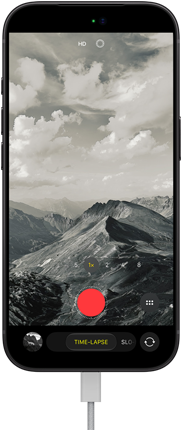 Smartfon z wyświetlaczem pokazującym czarno-białe zdjęcie gór, z widocznymi ikonami aparatu i przyciskiem nagrywania. Na ekranie znajduje się tekst: \'TIME-LAPSE\'.