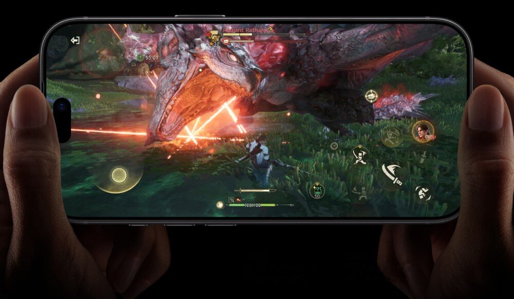 Smartfon APPLE iPhone 18 Pro Dwie dłonie trzymające smartfon w pozycji poziomej, na którego ekranie wyświetla się gra z postacią walczącą z wielkim smokiem