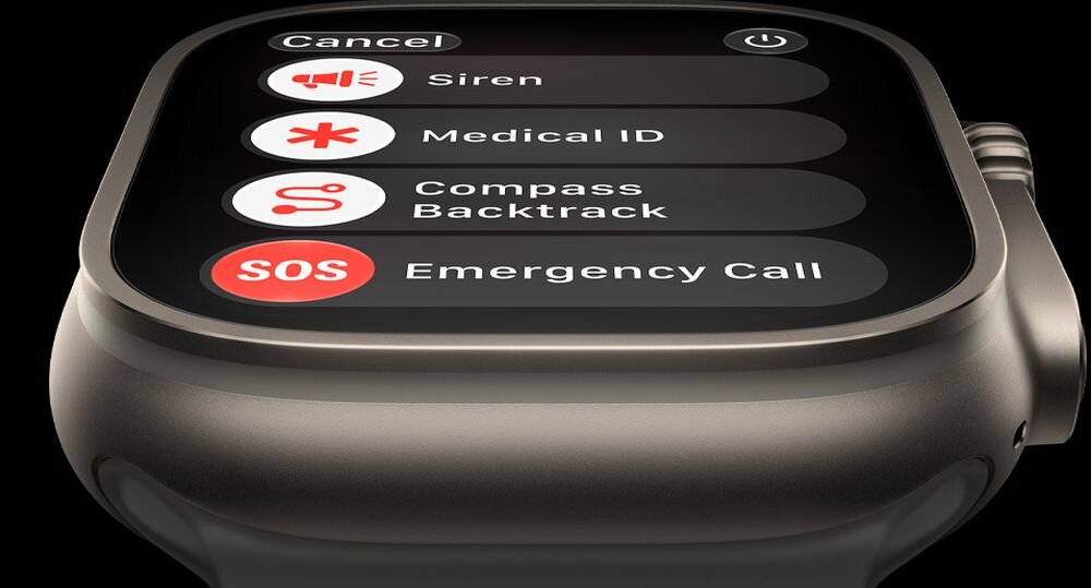 Zbliżenie na ekran zegarka z widocznymi opcjami: Cancel, Siren, Medical ID, Compass Backtrack, SOS Emergency Call. Obudowa zegarka jest metaliczna.