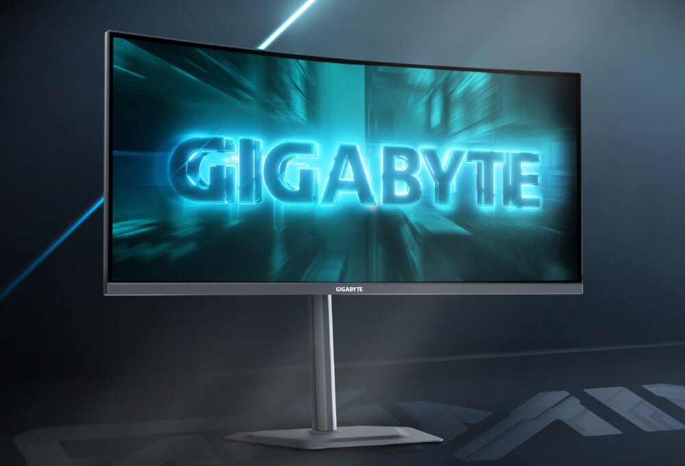 Monitor z zakrzywionym ekranem wyświetla dynamiczną grafikę z napisem \'GIGABYTE\'. Monitor stoi na prostym, metalicznym stojaku.