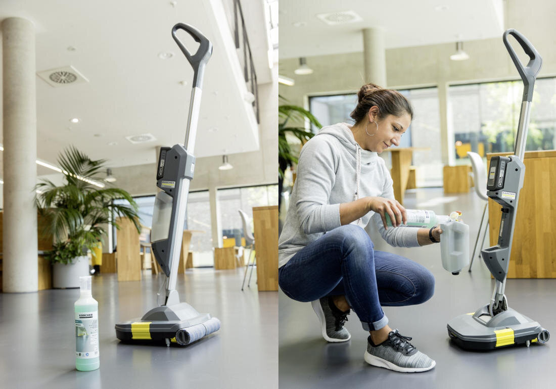 Na obrazie widoczna jest szorowarka kompaktowa z logo KARCHER, stojąca na podłodze w nowoczesnym wnętrzu z roślinami i drewnianymi elementami. Obok urządzenia znajduje się osoba w szarej bluzie, nalewająca płyn z butelki do pojemnika szorowarki.