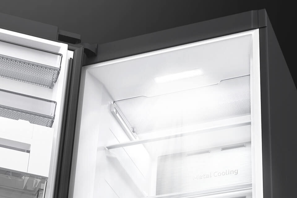 Wnętrze lodówki z widocznymi półkami i oświetleniem LED. Na tylnej ściance widoczny napis \'Metal Cooling\'.