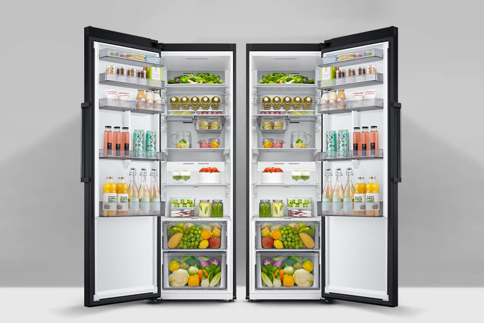 Dwie otwarte lodówki wypełnione różnorodnymi produktami spożywczymi, takimi jak owoce, warzywa, napoje i słoiki. Wnętrza lodówek są jasno oświetlone, a produkty są starannie poukładane na półkach i w szufladach.