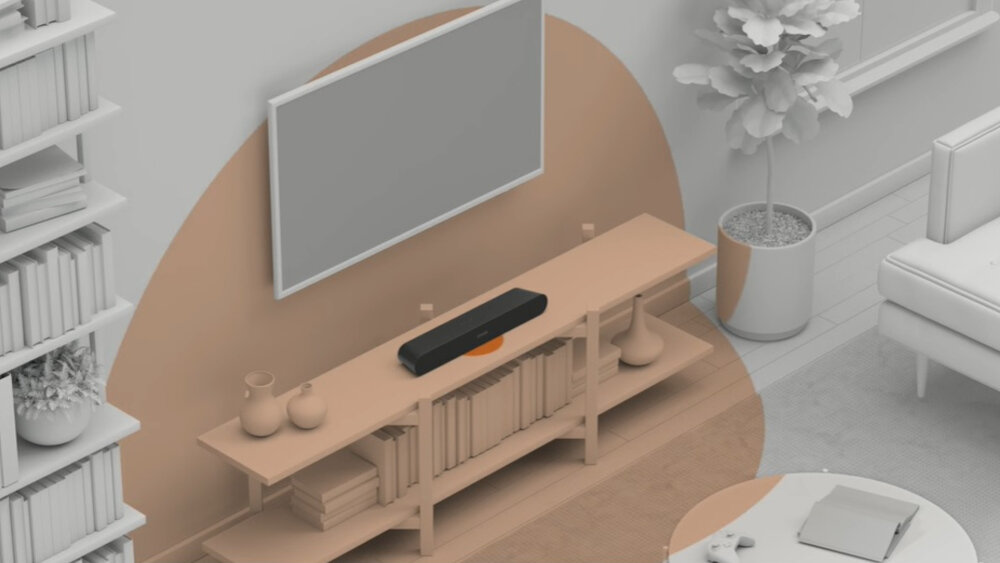 Na drewnianej półce pod telewizorem znajduje się czarny soundbar. W tle widać roślinę w doniczce oraz fragmenty mebli i książek.
