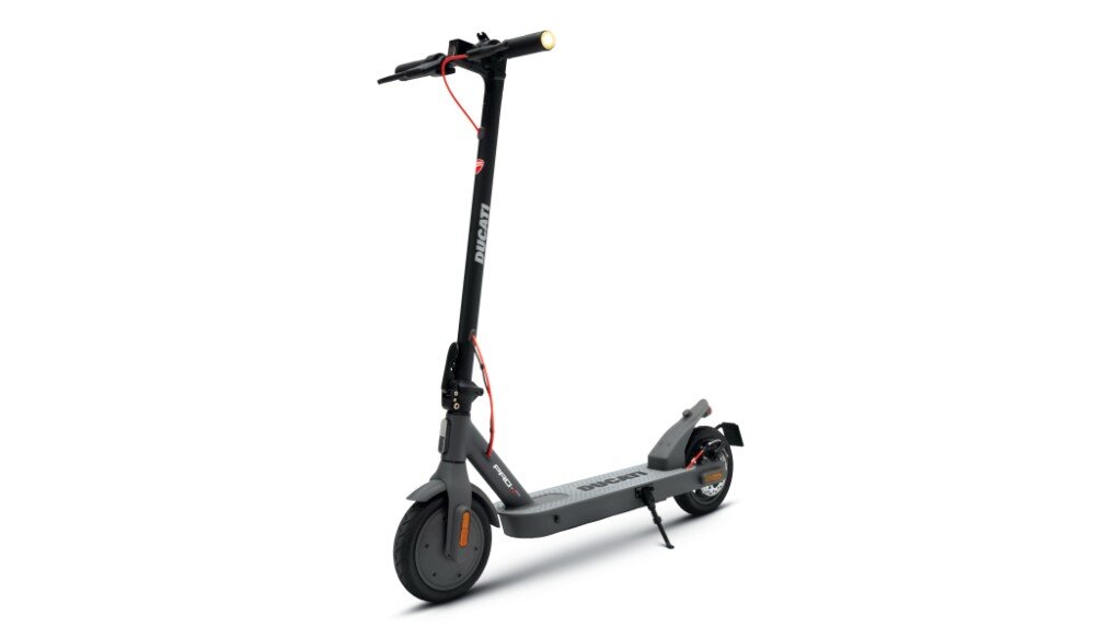Czarno-szara hulajnoga elektryczna z widocznym logo \'DUCATI\' na pionowej kolumnie kierownicy. Posiada czerwony przewód oraz przednie i tylne koła z pomarańczowymi elementami.