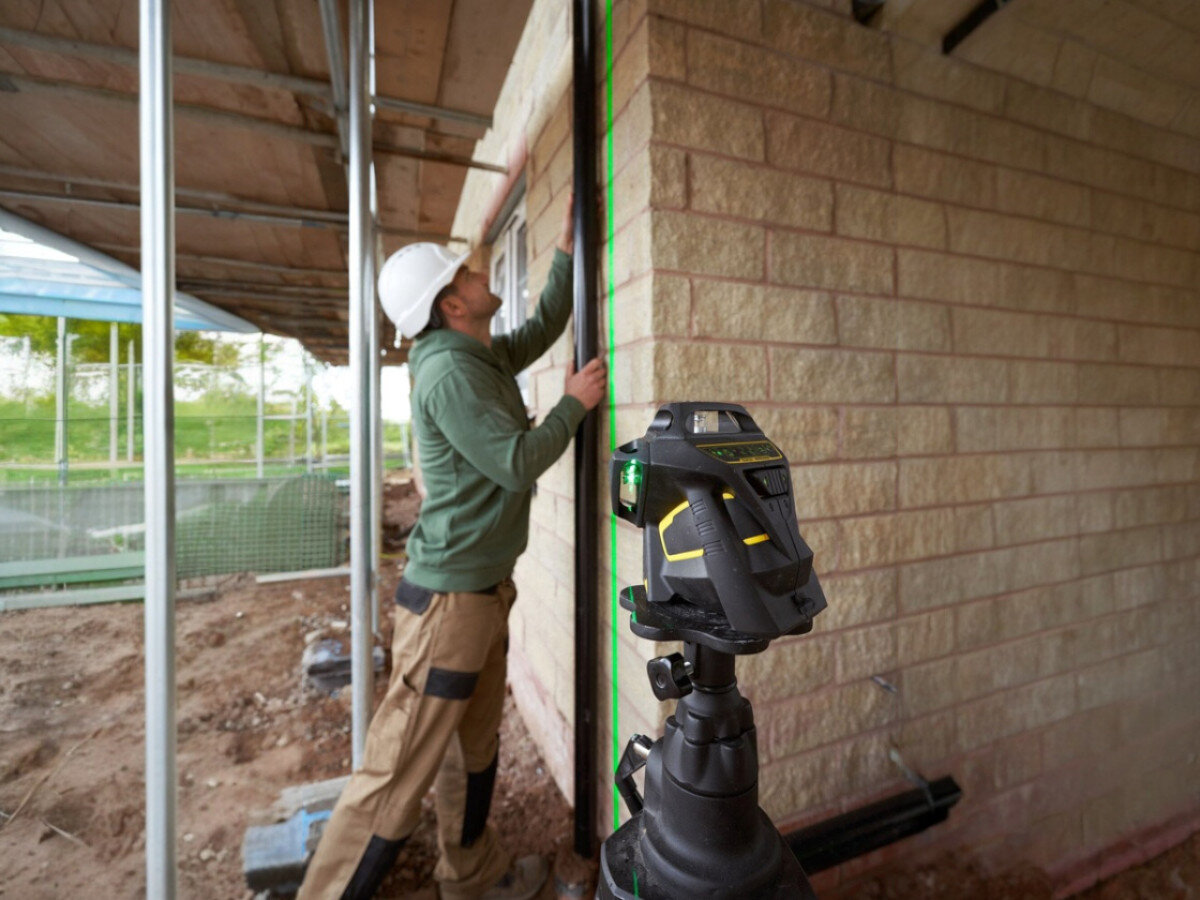 Laser krzyżowy STANLEY FatMax Multi-Line Laser 360, zasięg, wynik, pomiar, milimetr, mężczyzna pracuje na budowie, na pierwszym planie laser ze statywem