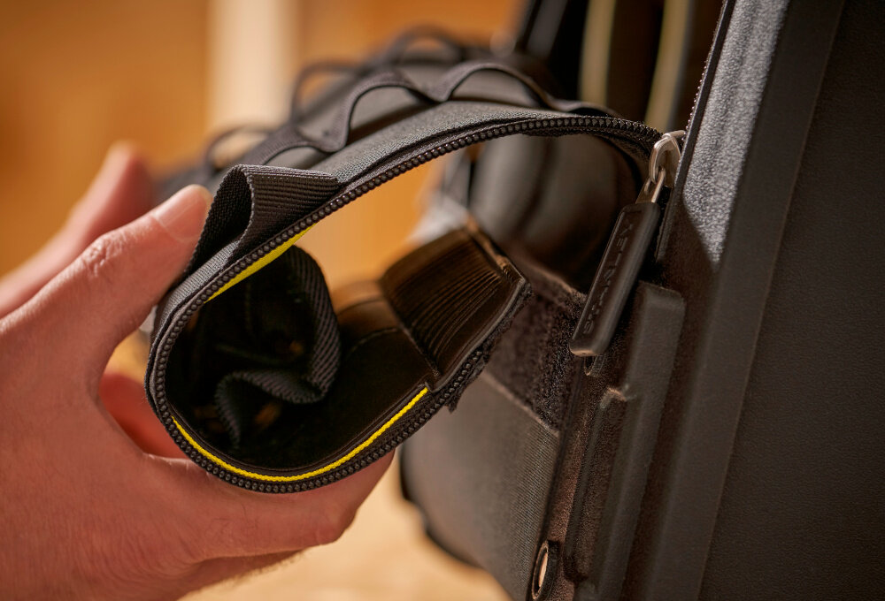 Torba narzędziowa STANLEY FatMax 1-94-231 pomieszczenie osoba trzyma pokrywę w dłoni mocuje ją na rzepie liczne przegródki rzep na pokrywie stabilne zamocowanie po zwinięciu metalowy zaczep