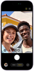 Smartfon z widocznym ekranem aplikacji aparatu fotograficznego. Na ekranie widoczny jest przycisk do robienia zdjęć oraz opcje \'VIDEO\' i \'PHOTO\'.