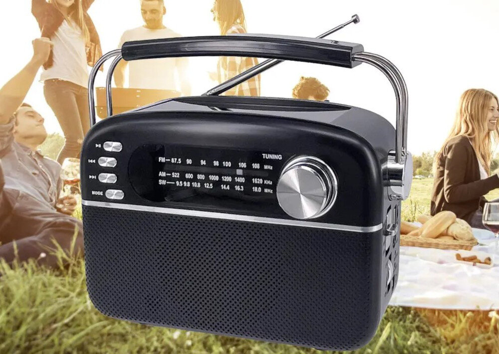 Czarne, przenośne radio z analogowym tunerem FM/AM/SW i dużym pokrętłem do strojenia. W tle widoczni są ludzie na pikniku.
