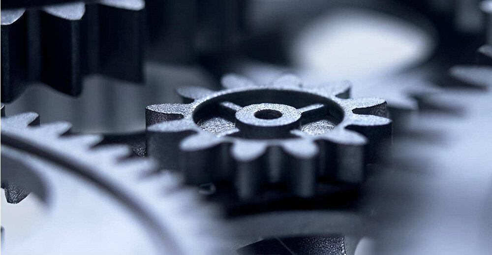 Zbliżenie na metalowe zębatki, które są częścią mechanizmu. Zębatki mają różne rozmiary i są ustawione w sposób sugerujący ich współpracę.