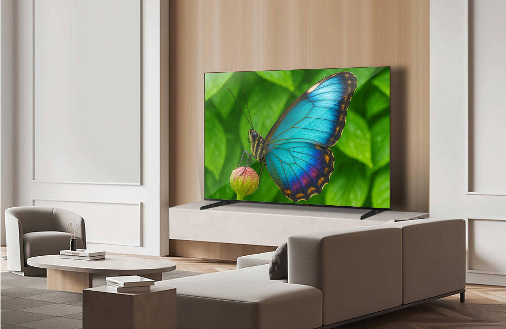 Telewizor wyświetla obraz motyla na tle zielonych liści. Wnętrze jest nowoczesne, z jasnymi ścianami i eleganckimi meblami.