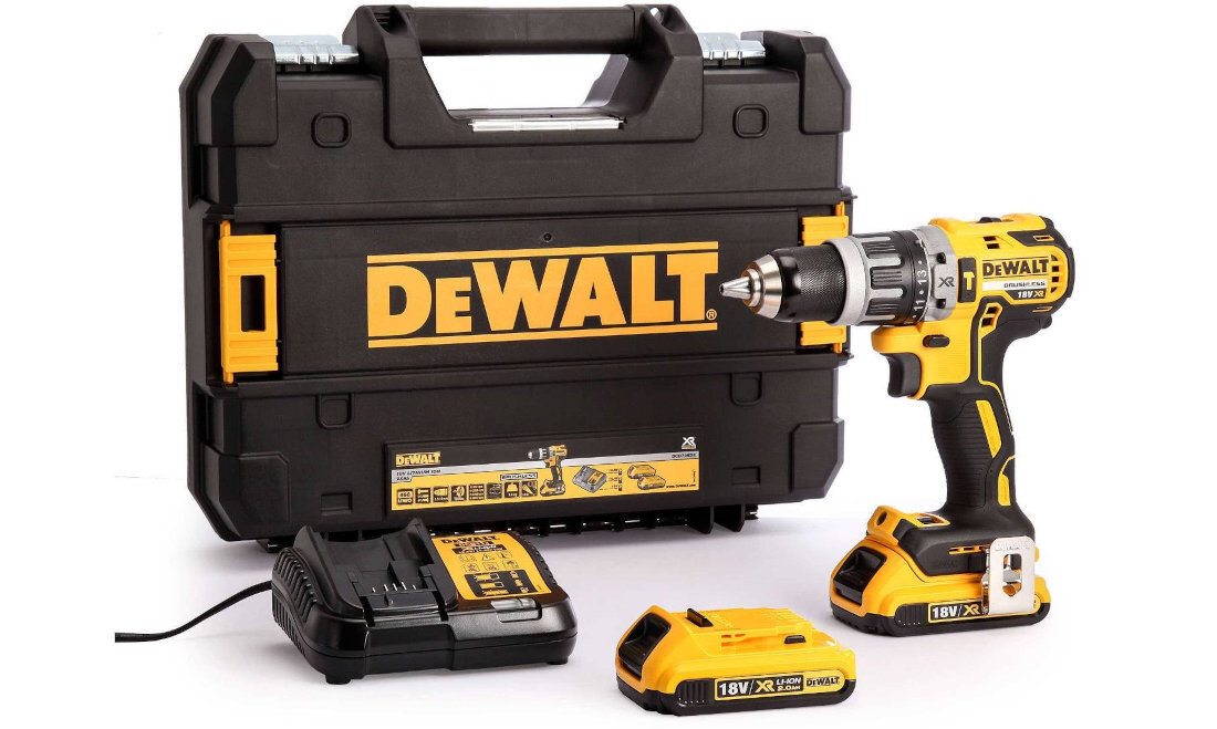 Na obrazie znajduje się wiertarko-wkrętarka w żółto-czarnych barwach, obok której leży ładowarka i akumulator. W tle widoczna jest czarna walizka z logo \'DEWALT\'.