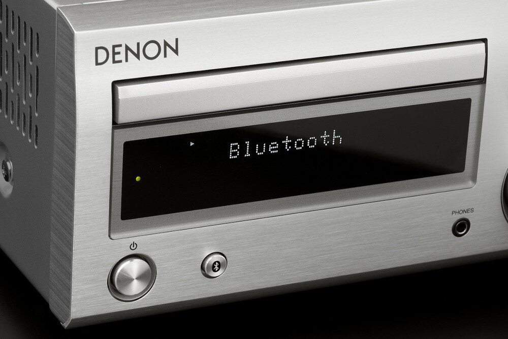 Srebrny amplituner z wyświetlaczem pokazującym tekst \'Bluetooth\'. Widoczne logo \'DENON\' oraz przyciski i pokrętła na panelu przednim.