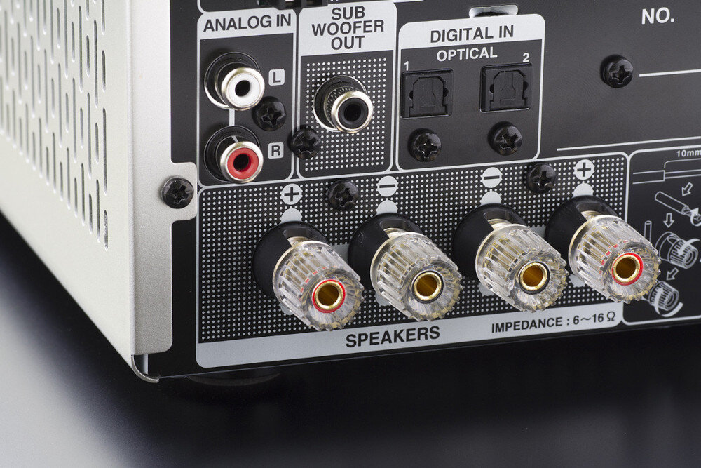 Tył amplitunera z widocznymi złączami: ANALOG IN, SUB WOOFER OUT, DIGITAL IN OPTICAL oraz SPEAKERS. Na dole napis: \'IMPEDANCE: 6~16Ω\'.