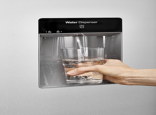 Osoba napełnia szklankę wodą z podajnika wody wbudowanego w lodówkę. Na panelu widoczny jest napis \'Water Dispenser\'.