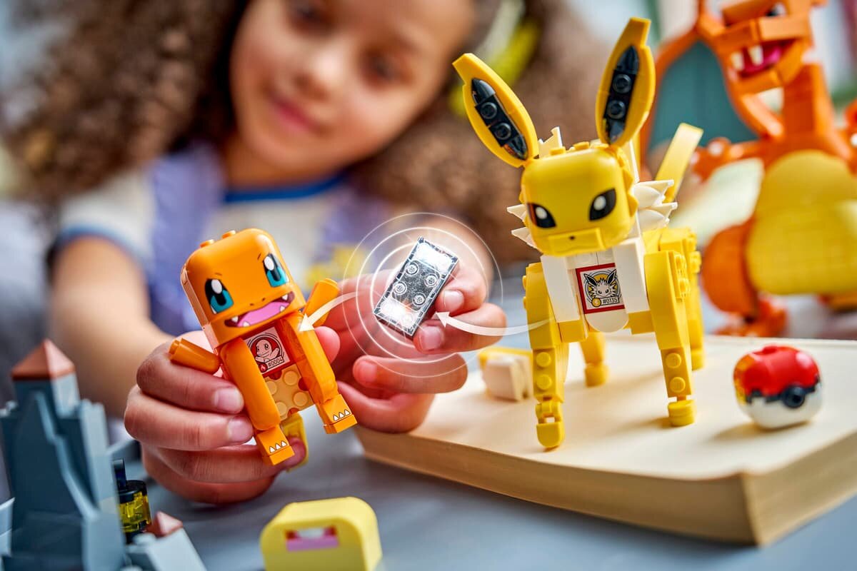 Na obrazie widać dziecko bawiące się figurkami LEGO przedstawiającymi postacie z Pokémon. W tle znajdują się inne elementy zestawu, w tym figurka przypominająca Poké Ball.