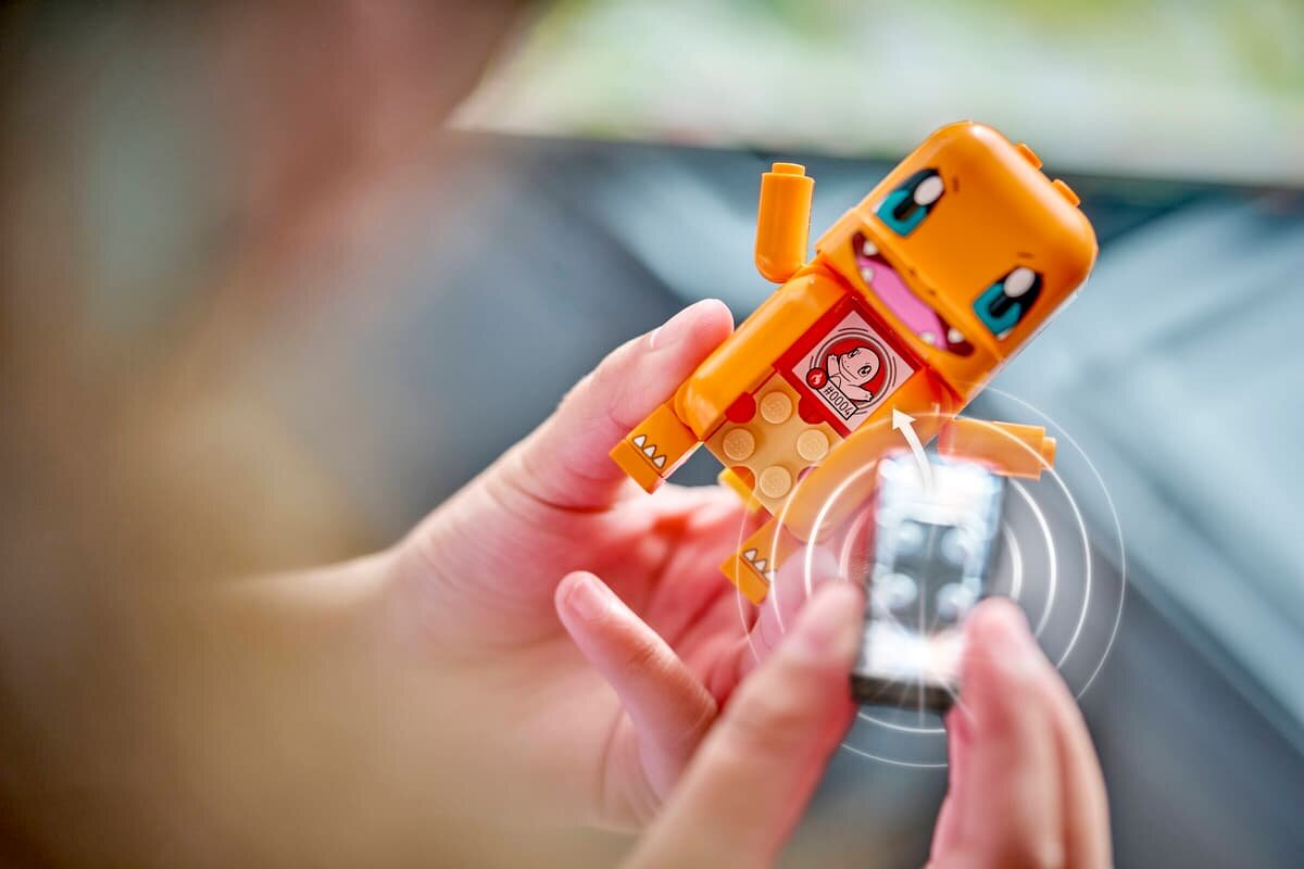 Osoba trzyma figurkę LEGO przedstawiającą pomarańczowego stwora z dużymi oczami i otwartymi ustami. Na figurce widoczny jest czerwony symbol z białym stworem.