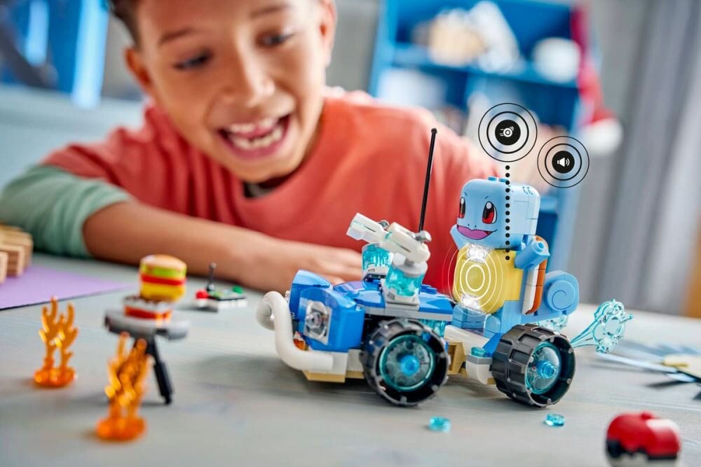 Na stole znajduje się zestaw LEGO z niebieskim pojazdem terenowym i figurką przypominającą Squirtle. W tle widać dziecko uśmiechające się do zabawki.