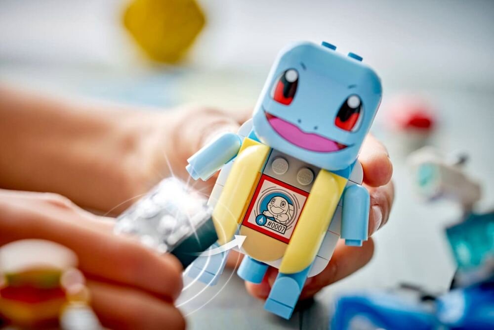 Na zdjęciu widać figurkę LEGO przedstawiającą postać Squirtle z serii Pokémon. Figurka trzymana jest w dłoni, a na jej brzuchu znajduje się naklejka z wizerunkiem Squirtle i tekstem \'00001\'.