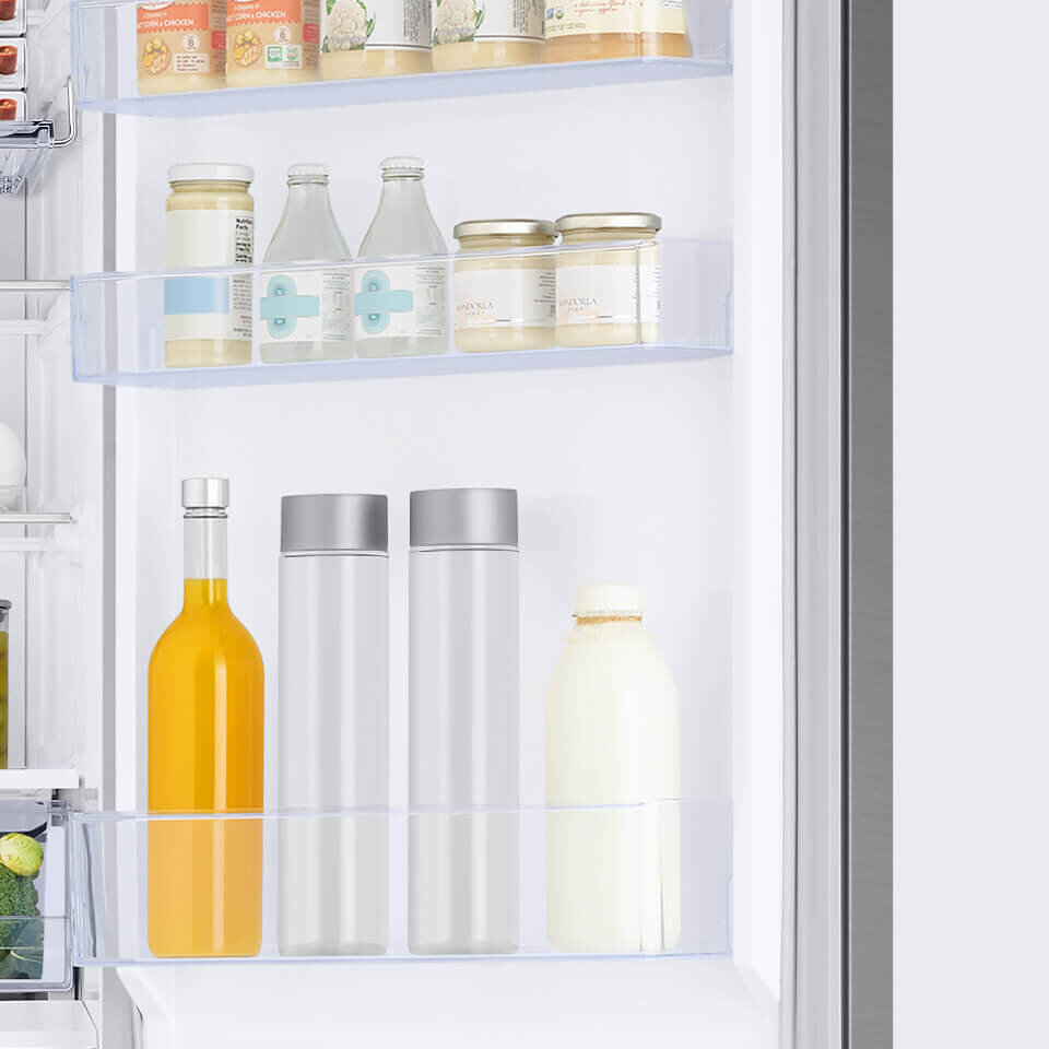 Dodatkowe miejsce na produkty Wnętrze lodówki z trzema półkami na drzwiach, na których znajdują się różne produkty spożywcze, w tym butelki i słoiki. Półki są przezroczyste, a produkty mają różne kolory i kształty.