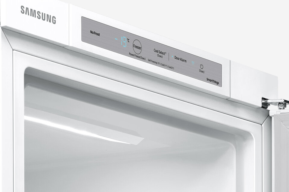 Biała zamrażarka z widocznym panelem sterowania, na którym znajduje się logo \'SAMSUNG\' oraz wyświetlacz pokazujący temperaturę -19°C. Na panelu widoczne są napisy: \'NoFrost\', \'Freezer\', \'Cool Select+\', \'Door Alarm\', \'SmartThings\'.