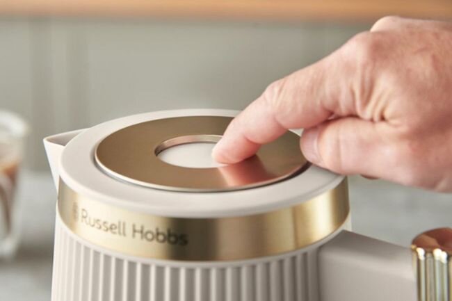Osoba naciska przycisk na górze urządzenia marki Russell Hobbs, które ma złote wykończenie.