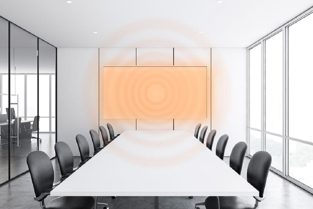 W nowoczesnym biurze znajduje się duży stół konferencyjny otoczony krzesłami. Na ścianie zamontowany jest panel grzewczy emitujący pomarańczowe fale ciepła.