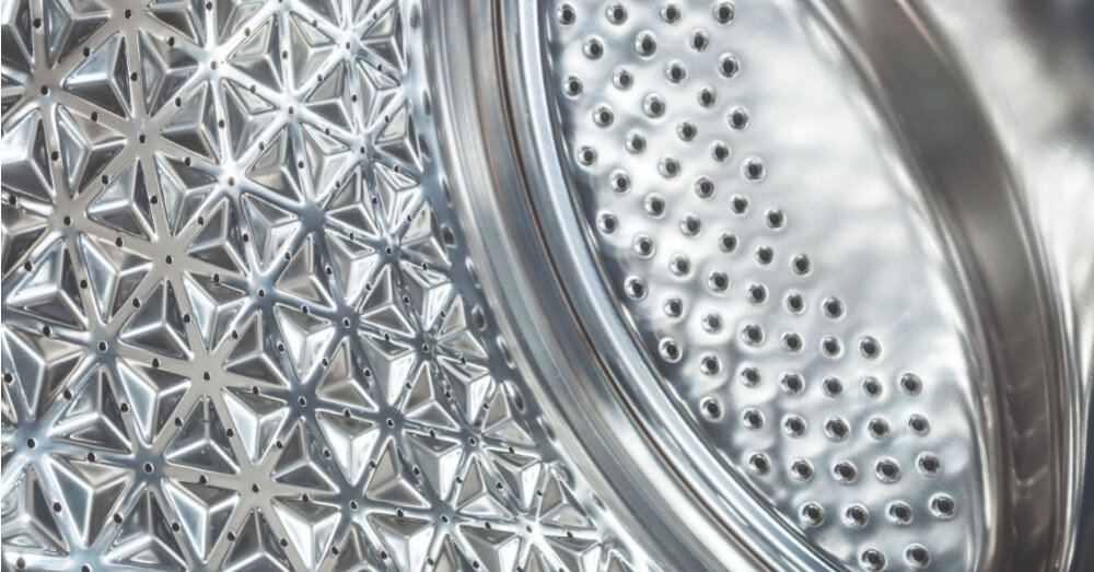 Zbliżenie na wnętrze bębna pralki z metaliczną powierzchnią pokrytą wypukłymi wzorami w kształcie gwiazd i kropek.